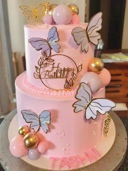 A lovely pink two-tier butterfly cake with gold and lavender butterflies, perfect for an elegant birthday.
