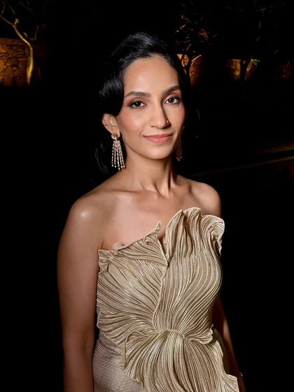 A portrait of elegance. The makeup is kept clean and luminous, focusing on flawless skin and softly defined eyes to complement the dramatic outfit and hairstyle.