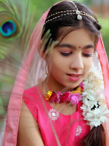 A close-up portrait of a girl in a Radha costume, featuring delicate floral jewelry and a pink veil for a soft, ethereal look.