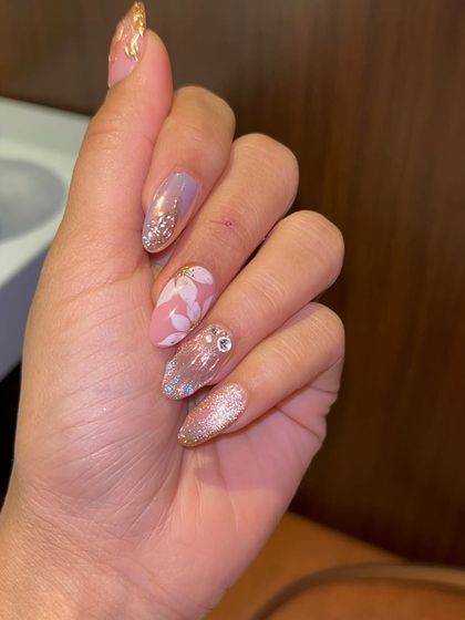 A soft and glamorous set with a mix of textures and finishes. It includes pink floral nails, glitter ombré, gold foil, and sculpted shell details for a multi-dimensional and feminine look.
