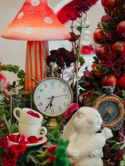 A detailed centerpiece featuring a vintage clock, stacked teacups, a white rabbit, and an apple tree, referencing key elements from the story.