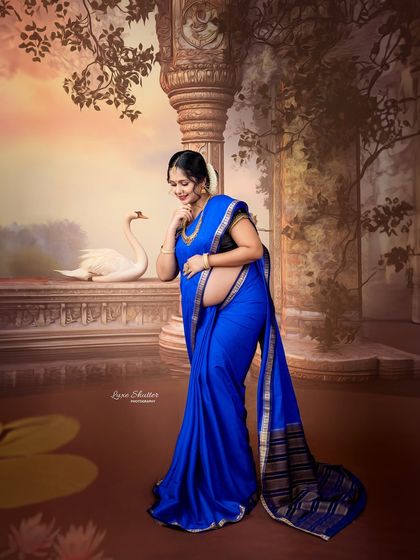 A serene and graceful portrait of a mother-to-be in a beautiful blue saree. The painterly background with ancient pillars and a swan adds a mythical, timeless quality.