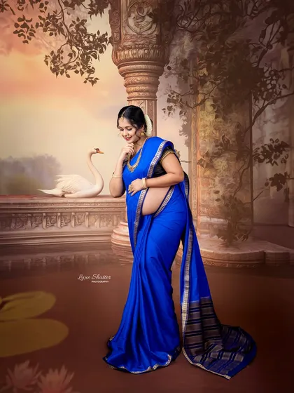 A serene and graceful portrait of a mother-to-be in a beautiful blue saree. The painterly background with ancient pillars and a swan adds a mythical, timeless quality.
