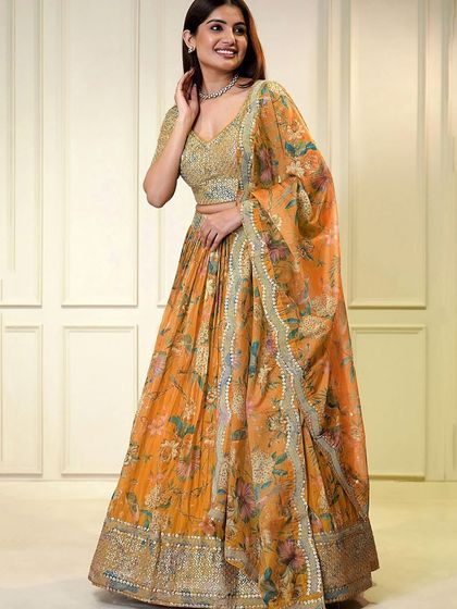 A pop of color for your celebration. This orange organza lehenga with a sequined blouse and floral skirt is designed for a fun and festive event like a Haldi or Sangeet.