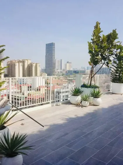 A wide view of a rooftop terrace garden overlooking the city. The design uses large white planters to create defined zones and add a modern touch.