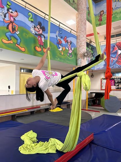 A young student practices a graceful backbend, using the silks for support to achieve a deeper and more controlled stretch.