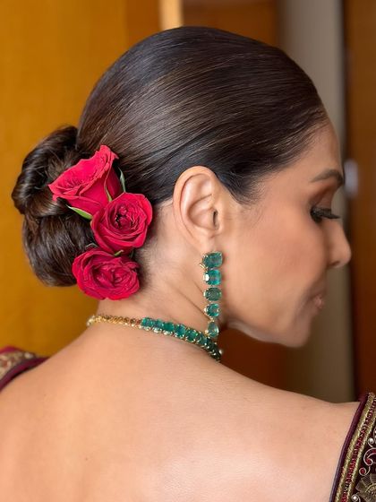 A detailed shot of the elegant hair styling. A sleek, low bun adorned with fresh red roses is a timeless choice that complements a bold makeup look perfectly.