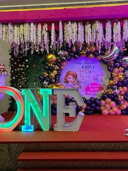 A large stage setup for a first birthday, featuring light-up "ONE" letters and a "Sofia the First" themed backdrop.