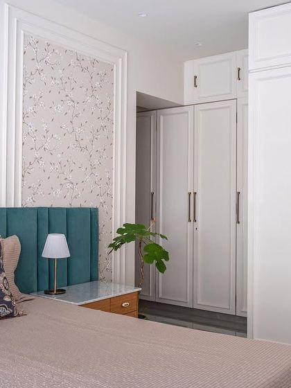 This grandparents' room emphasizes neutral colors, simplicity, and elegance. A champagne gold floral wallpaper and a teal green headboard create a sophisticated bed wall, while the white wardrobes with moulding add a perfect sheen to the space.