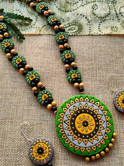 This is a long, 'haram' style necklace with a beautiful green, gray, and yellow mandala-designed pendant. The chain is made of matching smaller floral beads.