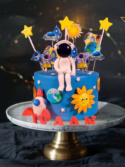 A cosmic adventure on a cake. This space-themed creation features an astronaut, a rocket, the sun, and planets, perfect for a stellar birthday.
