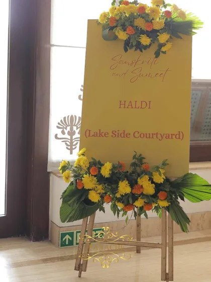 A simple yet elegant welcome sign for a Haldi ceremony at a lakeside courtyard, adorned with fresh marigolds and lush greens.