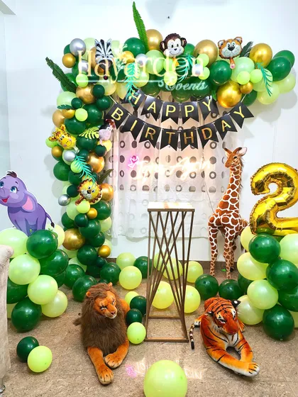 A lush jungle theme setup perfect for a home party. This decor is filled with green balloons, stuffed animal props like a lion and tiger, and a large giraffe.