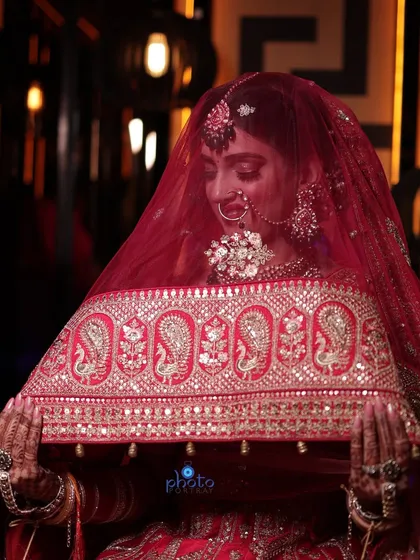 A traditional bridal pose with the bride holding her veil. This shot highlights the intricate embroidery of the dupatta and the bride's serene expression.