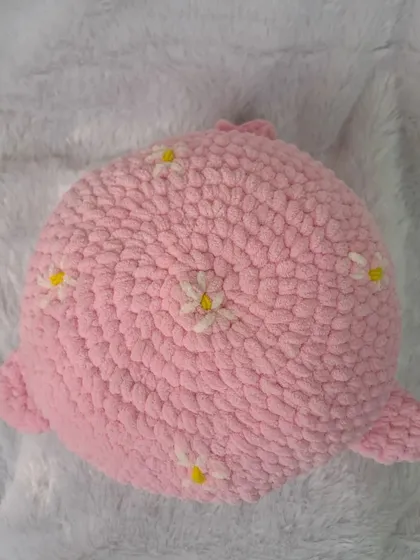 A top-down view of my pink whale pillow, showing the circular shape and the sweet, scattered daisy embroidery.