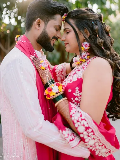 An intimate close-up where the focus is entirely on the couple's connection. The floral jewelry and bright pink outfits add to the celebratory feel of their pre-wedding ceremony.