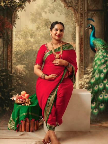 A regal portrait of a mom-to-be in a red saree, seated with a peacock in the background. This is a perfect example of a classic, painterly maternity photo.