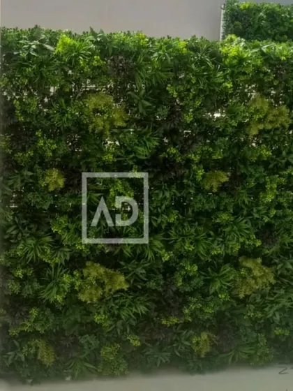This vertical garden uses a mix of light and dark green foliage with subtle yellow-green accents, creating a natural, sun-dappled look on a flat wall.