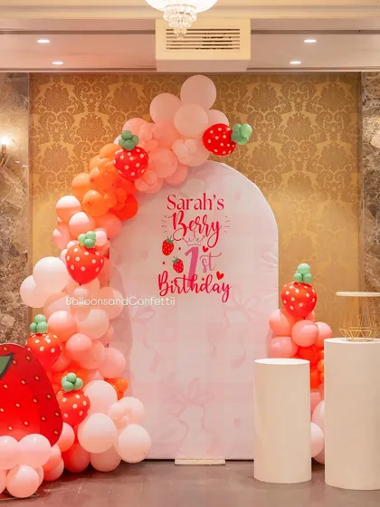 A closer look at the custom 'Sarah's Berry 1st Birthday' backdrop, framed by an adorable strawberry-themed balloon arch.