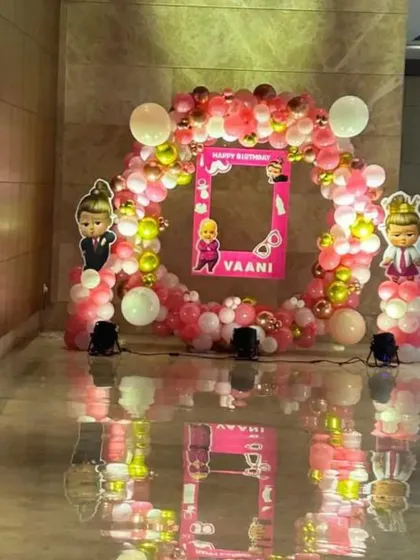 A Boss Baby theme for a baby girl's birthday party. This setup features a circular balloon arch in pink, white, and gold, with character cutouts and a personalized photo frame prop for guests.
