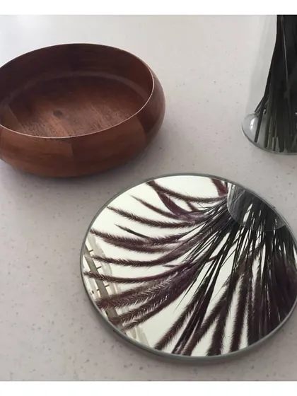 Reflections of peace. A simple composition on a dining table with a wooden bowl, a small mirror, and dried grasses creates a moment of calm and natural beauty.