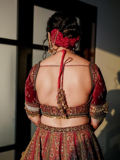 A back view of the bride's velvet lehenga, showing the full glory of the intricate red floral hair arrangement.