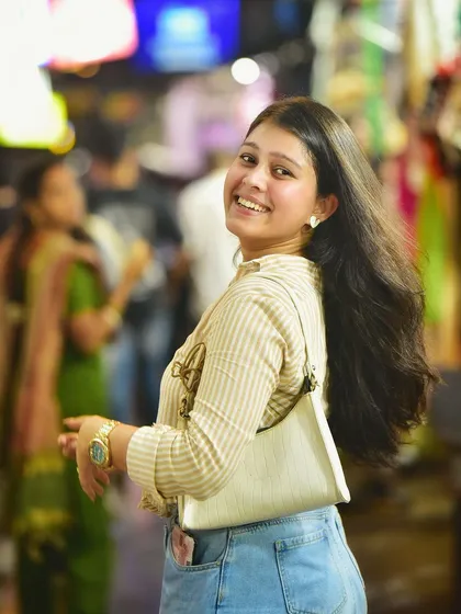 A joyful, candid portrait taken in the lively streets of Majnu Ka Tila at night. The motion in her hair and her bright smile capture a moment of pure happiness.