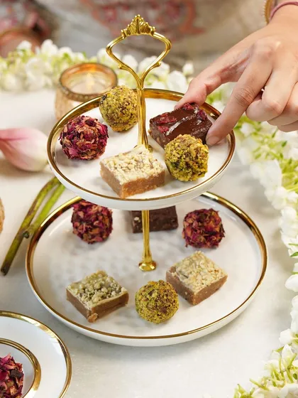 An elegant close-up of a tiered stand with vegan Diwali mithai, styled with flowers and diyas for a traditional yet modern look.