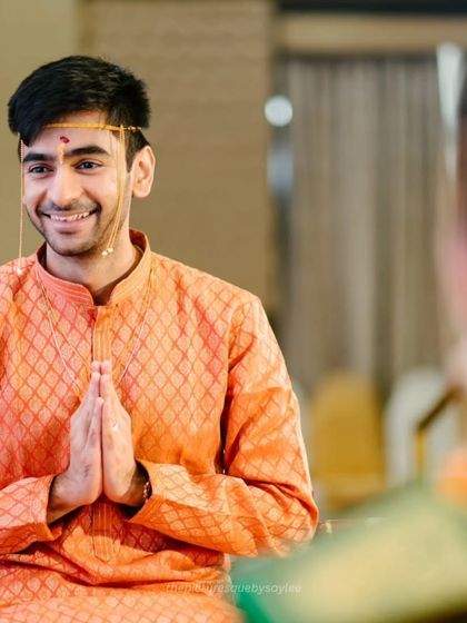 A candid shot of the groom with a welcoming smile and hands joined in 'namaste' during the wedding rituals.