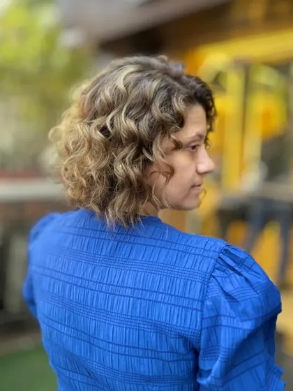 A side profile of a curly bob with bold color. This look is all about texture and dimension, with the highlights enhancing the natural curl pattern.