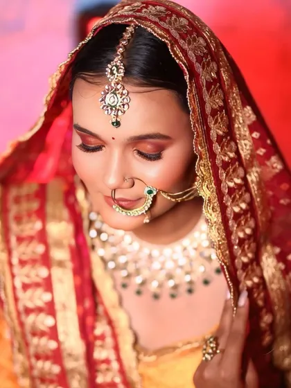 A close-up with the dupatta, showing the beautiful details of the eye makeup and the traditional nath. This is a classic North Indian bridal pose.