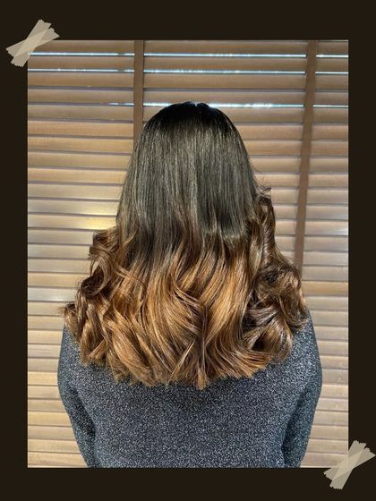 A back view of a beautiful balayage, showing the expert blending of colors from a dark base to warm, honey-blonde ends, styled in classic curls.