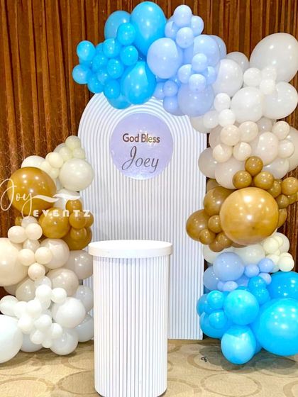 A simple and sweet stage decoration for a First Holy Communion. We used a balloon arch in shades of blue, brown, and white to frame a personalized backdrop and a single white plinth.