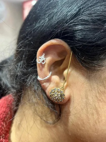 A spiritual and chic ear stack combining a silver Om hanging with a curved bar and a large gold floral stud.
