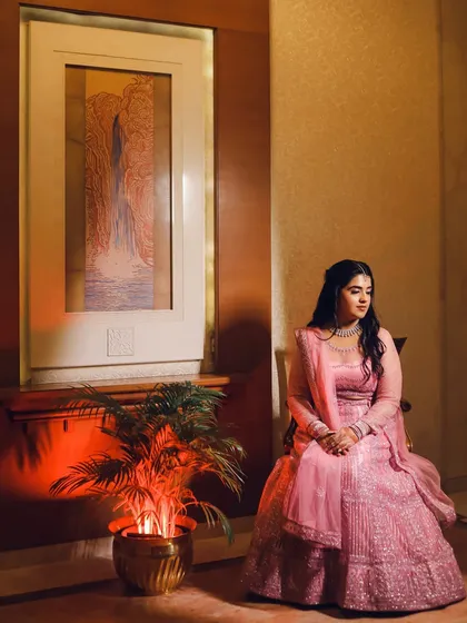 A seated portrait of the bride, her pink lehenga spread around her. She looks calm and graceful in this beautifully lit, elegant shot.