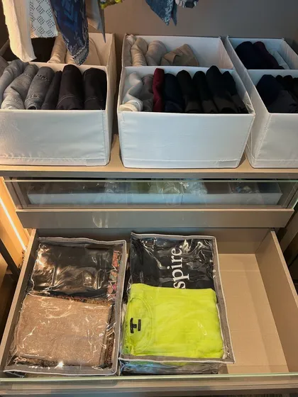 A look inside a drawer showing winter wear stored in clear protective bags, while the shelf above holds neatly folded sweaters in bins.