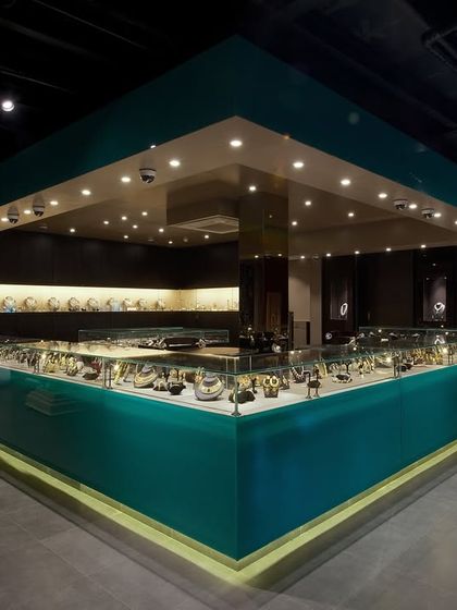 This image from 'The Big Door' showcases the retail display, designed as a jewel box. The turquoise, high-gloss counter and focused overhead lighting make the products the center of attention, creating a luxury shopping experience.