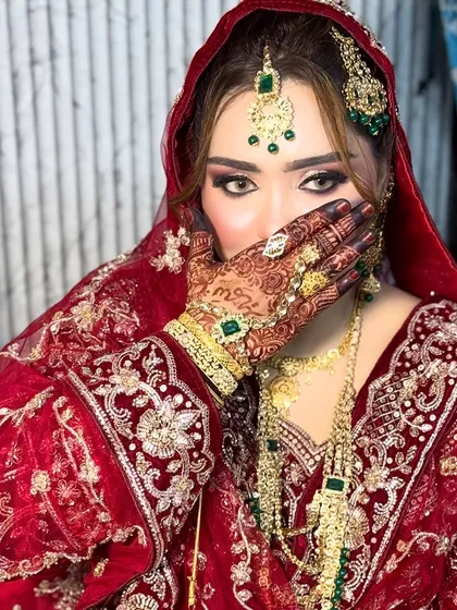 A classic pose for a classic Nikkah bride. This shot highlights the intricate henna and the dramatic eye makeup with bold liner and lashes. The combination of the red and green in her outfit and jewelry is a timeless choice.