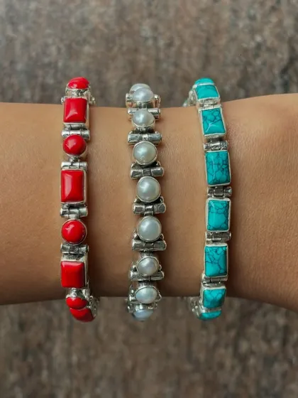 A stack of three of our popular stone bracelets. This image showcases the vibrant red coral, classic white pearl, and serene blue turquoise options, all set in sterling silver.