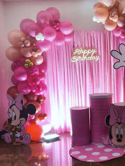 A closer look at the details of the Minnie Mouse party setup. You can see the neon "Happy Birthday" sign, the custom-wrapped pedestals for the cake, and the organic balloon arch with varying shades of pink.