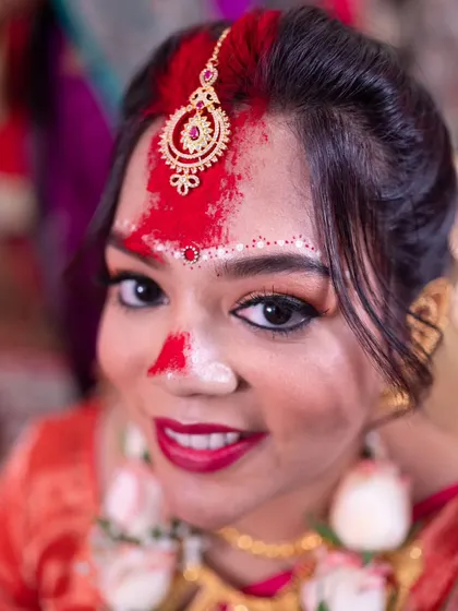 A bright and happy portrait of a Bengali bride, her face adorned with sindoor, smiling for the camera.