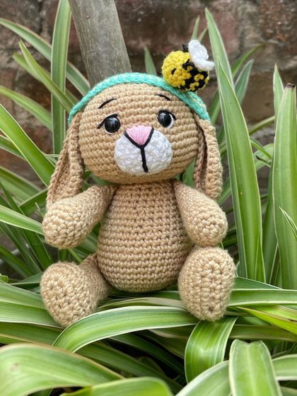 This is Oliver the Bunny, a sweet little friend with a bee named Bob on his headband. He's sitting patiently among the leaves.