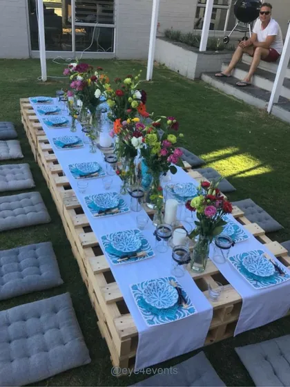 We bring the party to your backyard with our casual outdoor picnic setups. This arrangement uses low pallet tables, comfortable grey floor cushions, and vibrant floral centerpieces for a relaxed and colorful garden party.