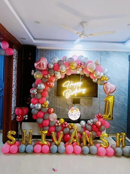A glamorous first birthday setup in pink, grey, and gold, with a neon sign and foil letters spelling the name.