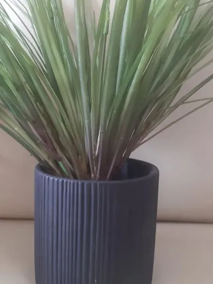 A simple yet elegant black ceramic planter with a vertical ribbed texture. It's a versatile piece that works well for holding artificial grasses or succulents in a modern setting.