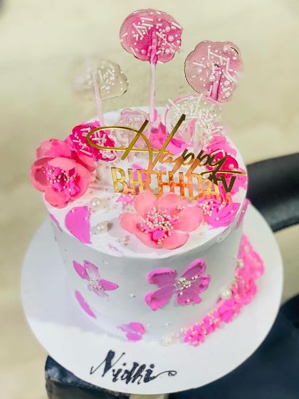 A pretty pink cake with lollipops and floral decorations, perfect for a sweet celebration.