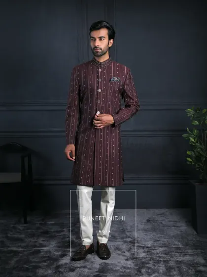 An ode to Indian elegance. A wine Achkan in deep maroon, adorned with pintucked textures and statement metallic buttons, draped with a stole enriched in geometric finesse.