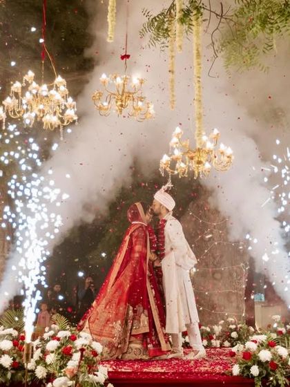 A spectacular Varmala moment with the couple surrounded by cold pyro fireworks. The backdrop is a lush garden setting with trees adorned with chandeliers.