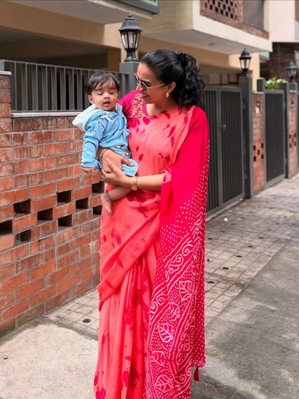 This photo combines my love for sarees with my role as a mom. I'm holding Gauri while wearing a lovely red tie-dye saree, showing that traditional wear can be practical and beautiful for everyday mom life.