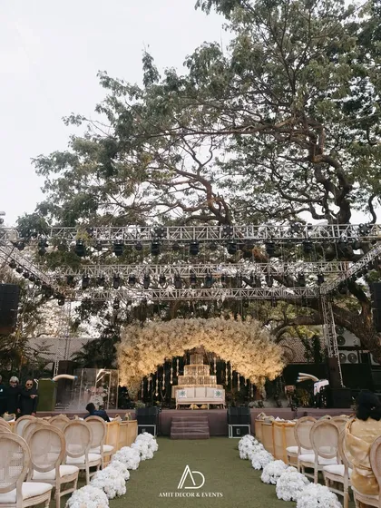 A view down the aisle towards the grand floral stage. The aisle is lined with white flowers, leading the eye towards the beautifully lit focal point of the ceremony.